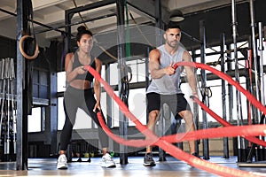 Athletic young couple with battle rope doing exercise in functional training fitness gym