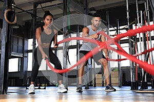 Athletic young couple with battle rope doing exercise in functional training fitness gym