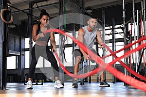 Athletic young couple with battle rope doing exercise in functional training fitness gym