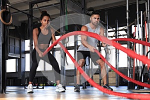 Athletic young couple with battle rope doing exercise in functional training fitness gym