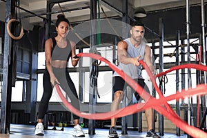 Athletic young couple with battle rope doing exercise in functional training fitness gym