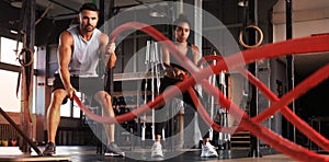 Athletic young couple with battle rope doing exercise in functional training fitness gym