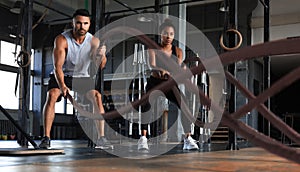 Athletic young couple with battle rope doing exercise in functional training fitness gym