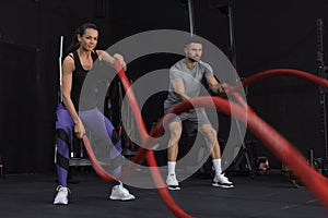 Athletic young couple with battle rope doing exercise in functional training fitness gym.