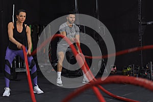 Athletic young couple with battle rope doing exercise in functional training fitness gym.