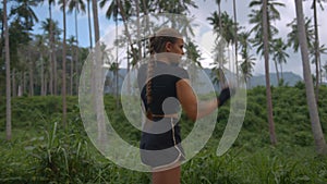Athletic young female in black sportsuit works out alone in tropical park in daylight shadowboxing