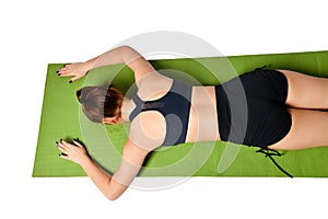 Athletic young girl lies face down on a yoga mat and stretches her arms forward in front of her.