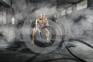 Athletic young man with battle rope doing exercise in the fitness gym