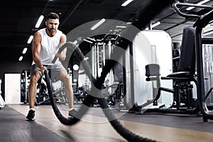 Athletic young man with battle rope doing exercise in functional training fitness gym