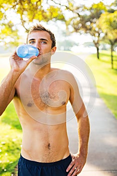 Athletic young man drinking water after workout