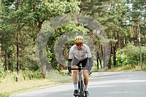 Athletic young man in outfit rides a bicycle in the summer outside the city in the woods on an asphalt road