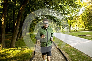 Athletic young man running while doing workout in sunny green park