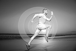 Athletic young man running in the nature. Fit man fitness model working outdoor by sea beach. Dynamic run movement.