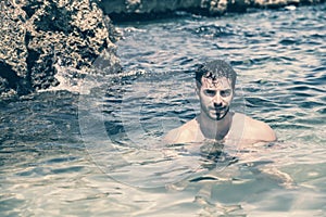 Athletic young man in the sea or ocean by rocks