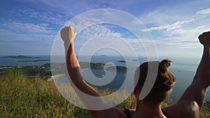 Athletic young man stands with his hands up on the edge of the mountain.