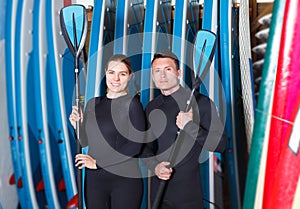 Athletic young people in wetsuits standing with surfboards