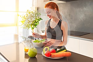 Athletic young red haired woman in the home kitchen eating a healthy salad