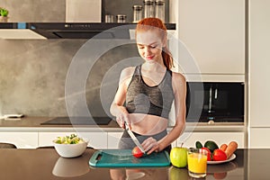 Athletic young red haired woman in the home kitchen prepares a vegetable centrifuged and a salad