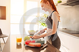 Athletic young red haired woman in the home kitchen prepares a vegetable centrifuged and a salad