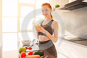 Athletic young red haired woman in the kitchen with a glass of fruit centrifuged juice