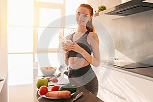 Athletic young red haired woman in the kitchen with a glass of fruit centrifuged juice photo