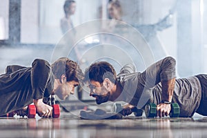 Athletic young sportsmen doing push ups with dumbbells at the gym