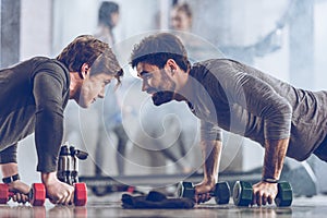 Athletic young sportsmen doing push ups with dumbbells at the gym