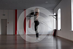 Athletic young woman in black sportswear jumps on a skipping rope and burns calories in a fitness studio. Girl in training