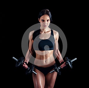 Athletic young woman doing a fitness workout against black background. Attractive fitness girl pumping up muscles with dumbbells.