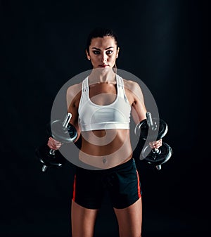 Athletic young woman doing a fitness workout against black background. Attractive fitness girl pumping up muscles with dumbbells.