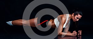 Athletic young woman doing planking exercise against black background. Sporty woman in sportswear with perfect fitness body.