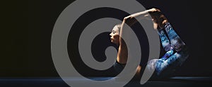 Athletic young woman doing yoga exercises. Black background, charming light, serene mood.