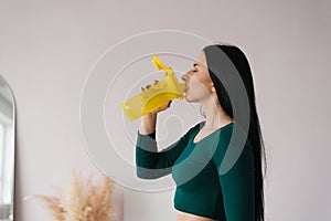 Athletic young woman drinks water from a yellow bottle after a workout at home