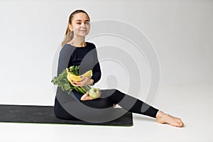 Athletic young woman holding vegetables in the gym on a white background. Diet food, weight loss