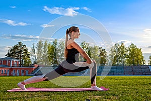 Athletic young woman in a sports dress doing fitness exercises. Yoga classes at the stadium