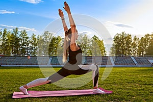 Athletic young woman in a sports dress doing fitness exercises. Yoga classes at the stadium