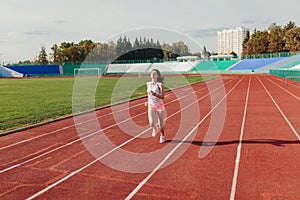 Athletic young woman in sportswear sprinting on running track stadium at sunset