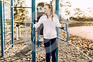 Athletic young woman in sportswear trains on a horizontal bar, in the morning in the fresh air