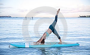 Athletic young woman in SUP Yoga practice side bend leg lift Pose in Ala Moana Hawaii