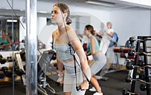 Athletic young woman using exercise machine with ropes at gym