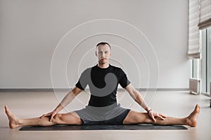 An athletically built man does yoga in the gym on a mat