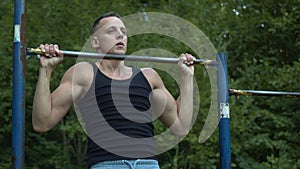 Athletically built man pulls up on the horizontal bar. Loads on different types of muscles. Bodybuilding. Outdoor sports