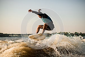 athlitic man energetically jumping on a wakesurf board over river waves