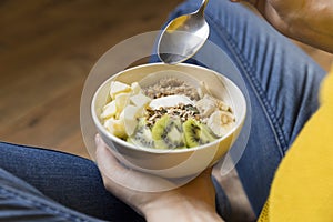 Ating healthy breakfast bowl. Yogurt, buckwheat, seeds, fresh fruits in white bowl in woman`s hands. Clean eating, dieting, detox