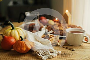 Atmospheric autumn still life. Pumpkins, warm tea in stylish cup on rustic wooden table with freshly baked apple pie with cinnamon