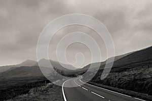 An atmospheric black and white edit of a road heading towards mountains on a stormy winters day. Snowdonia, Wales. UK.