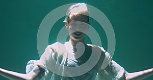 Atmospheric cinematic portrait, young beautiful short haired blonde woman posing, smiling deep under water slow motion.