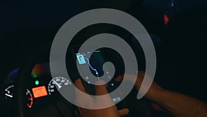 Atmospheric close-up shot of human hands driving in a car at night and holding smartphone with GPS navigation app map.