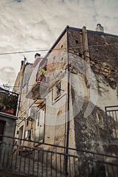 Atmospheric Italian Brick House with Balcony and Hanging Laundry Under Cloudy Sky in Rocca Imperiale