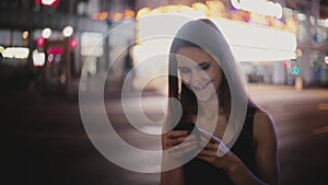 Atmospheric medium shot of happy Caucasian young local woman using smartphone app in dark New York night street smiling.